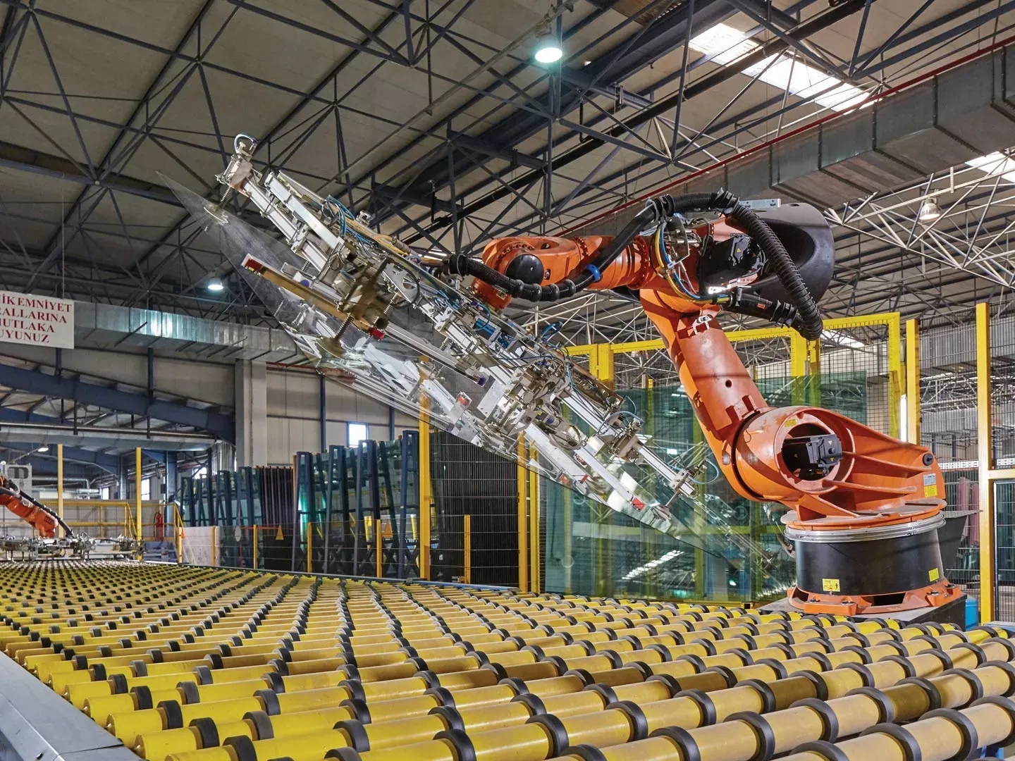 Industrial robot arm handling glass above a roller conveyor