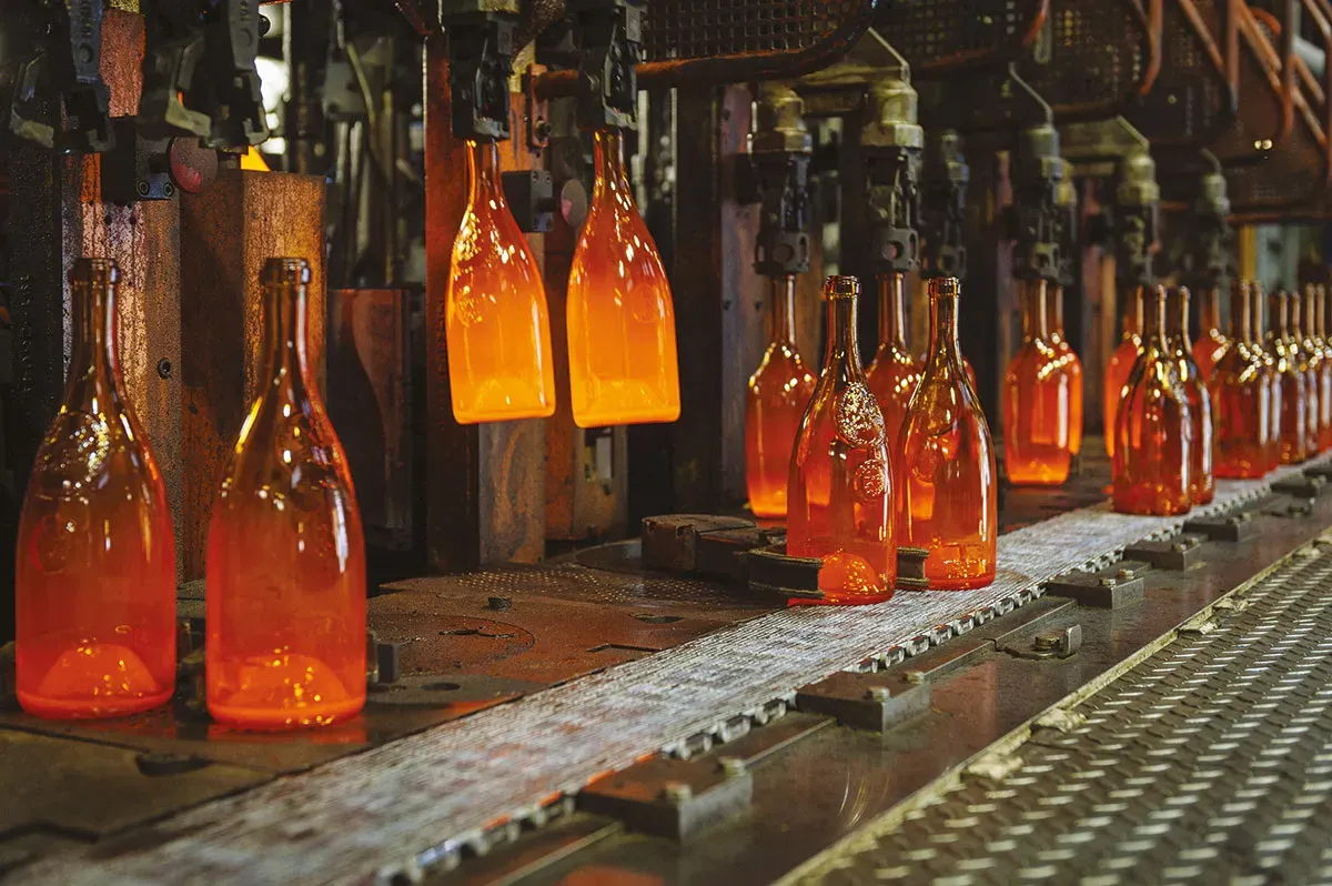 Glowing glass bottles leaving the forming machines at the hot end